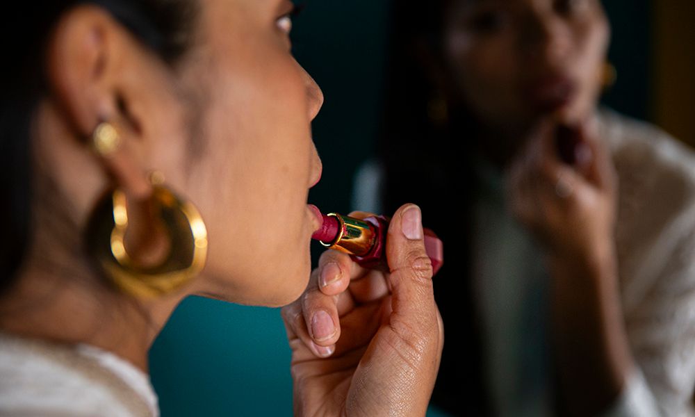 Woman applying lipstick in front of mirror