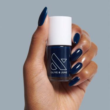 A close up image of a woman's hand holding a bottle of Olive & June navy nail polish