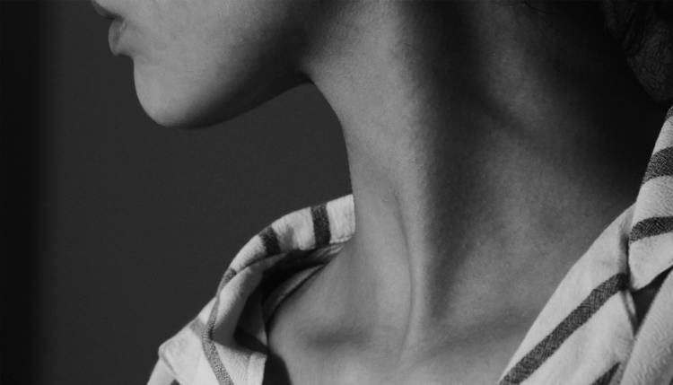 Black-and-white close-up of a person’s neck and jawline, with their head tilted upward and a striped shirt visible at the shoulders.