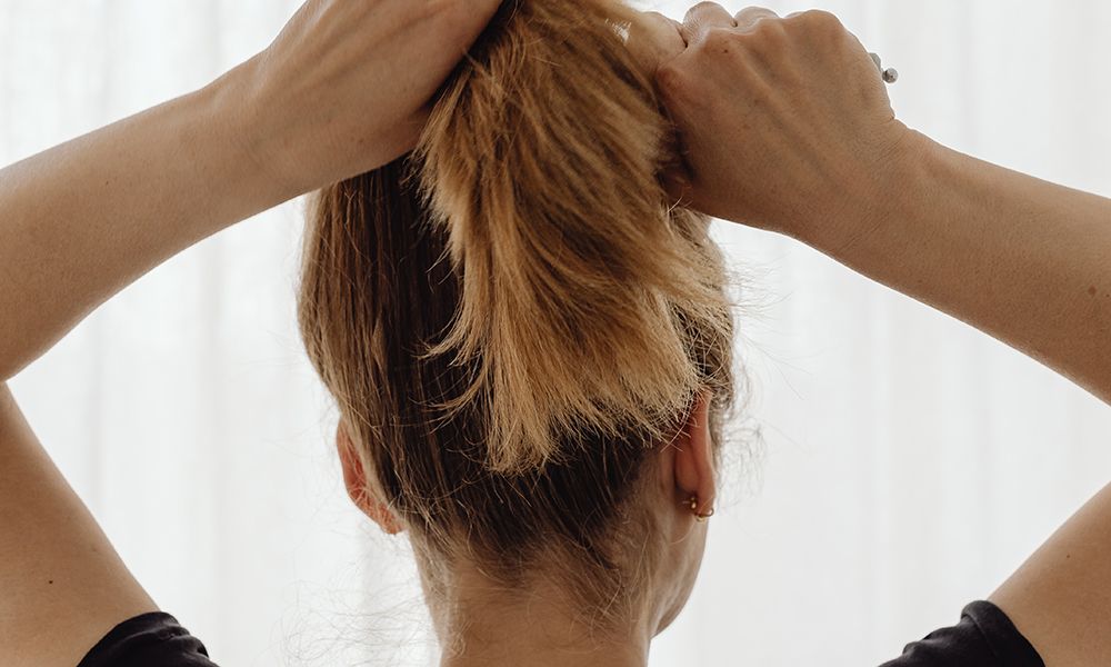 back view of woman putting hair into a ponytail