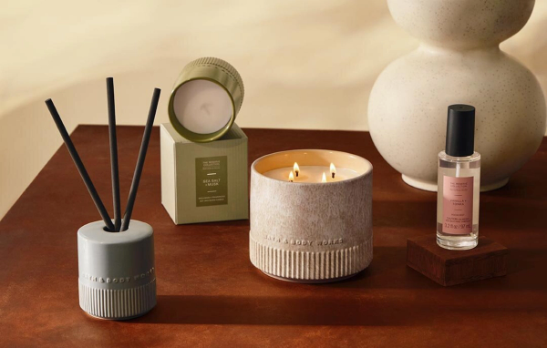 Bath & Body Works Reserve Collection products styled on a wooden table, including a lit three-wick candle, a reed diffuser, a boxed Sea Salt + Musk candle and a Vanilla + Tonka room mist.