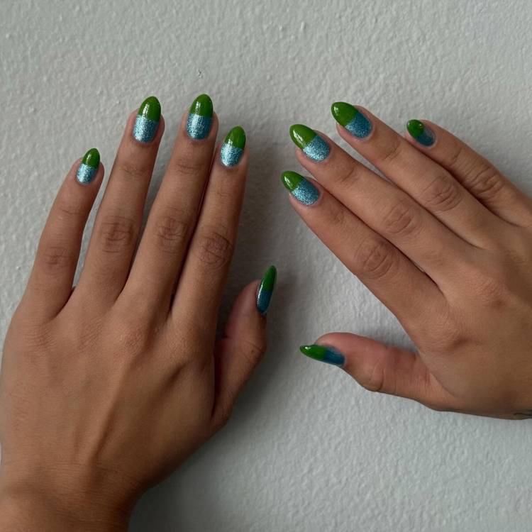 Hands with blue-green pill-box-inspired nails featuring metallic turquoise bases and glossy green tips against a pale wall.