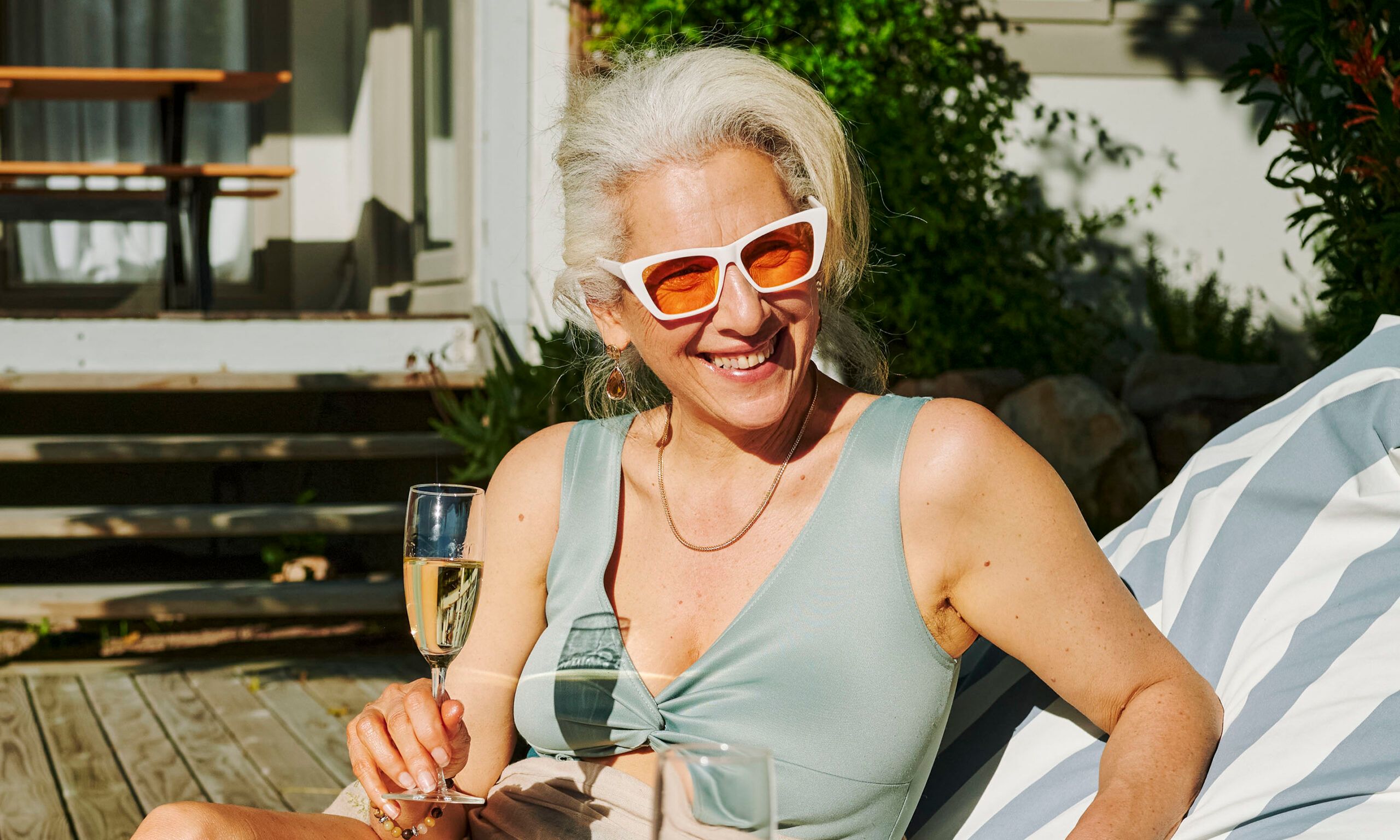 Two mature female friends in swimwear smiling and talking over glasses of champagne by the swimming pool at their accommodation during a weekend getaway in summer