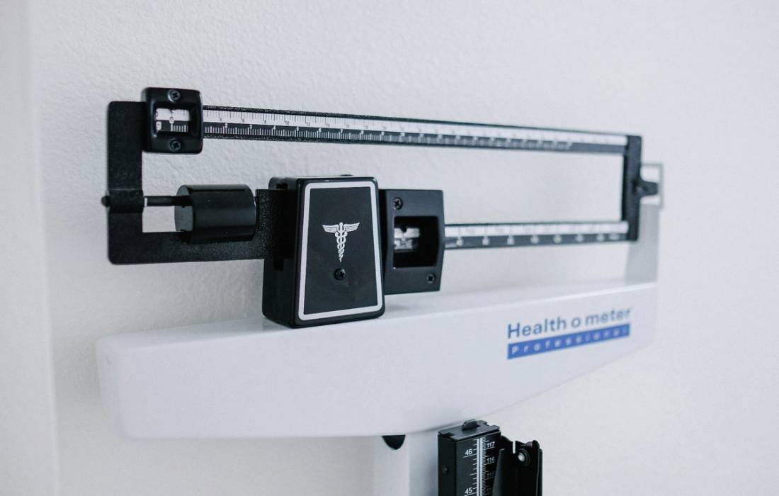 Close-up of a physician’s balance-beam scale against a white wall.