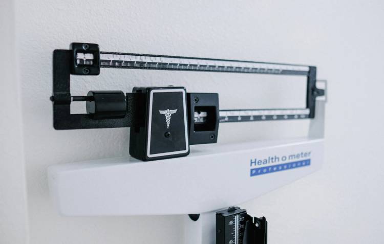 Close-up of a physician’s balance-beam scale against a white wall.