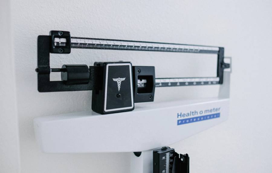 Close-up of a physician’s balance-beam scale against a white wall.