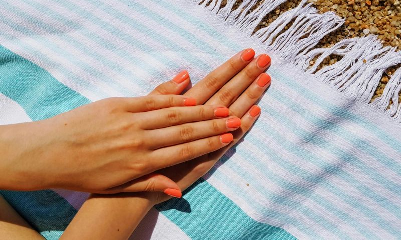 hands with orange nail polish on towel at the beach