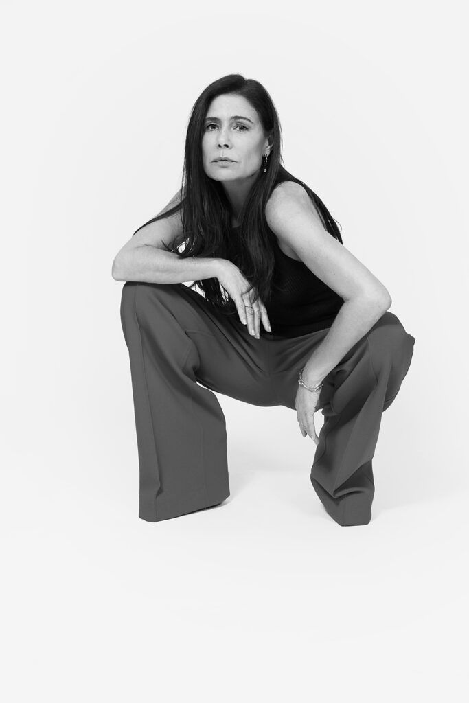 Black and white photo of Maura Tierney crouching on white background