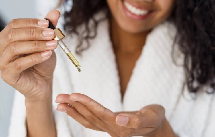 Smiling woman holding a dropper of facial serum above her open palm.