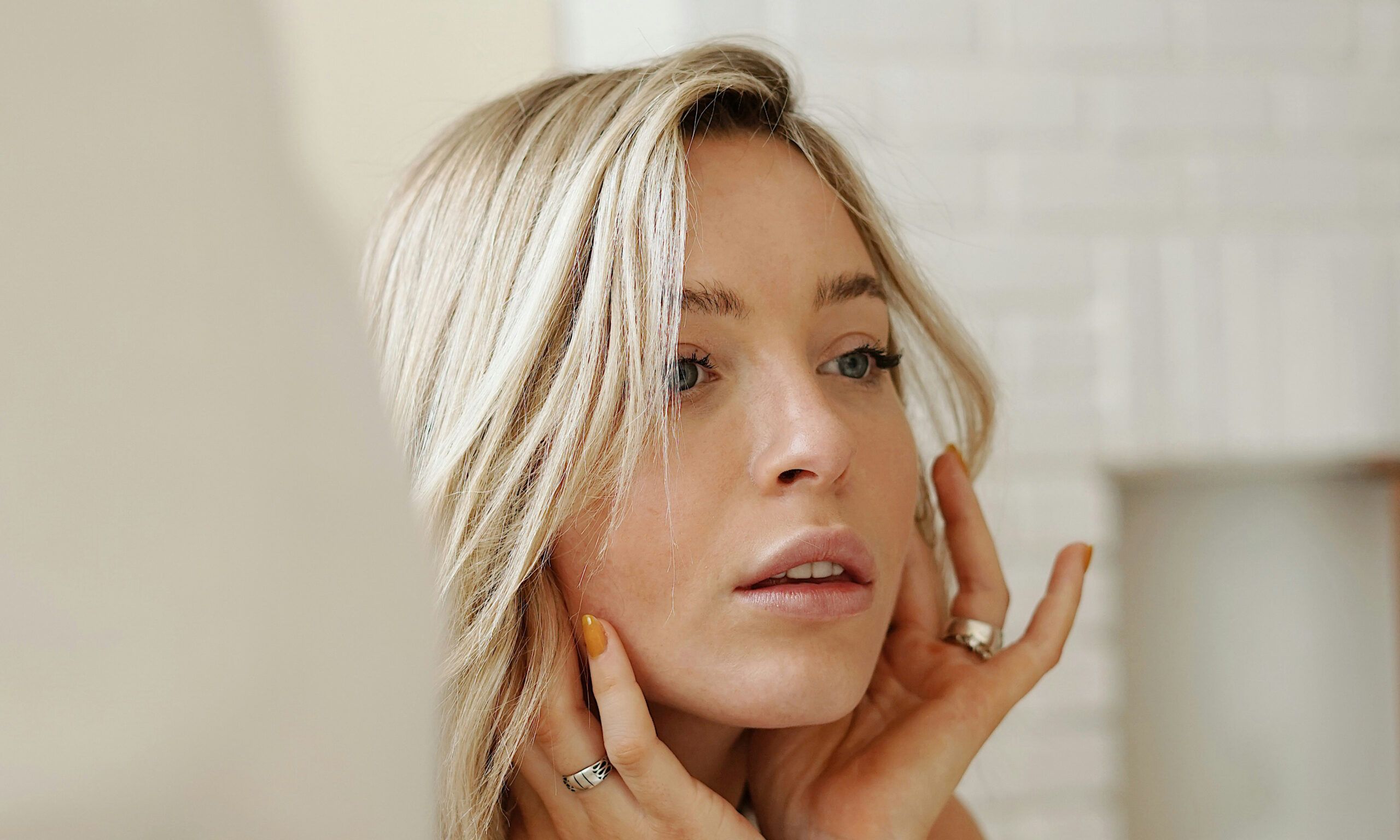 Woman with short blonde hair looking at face in mirror