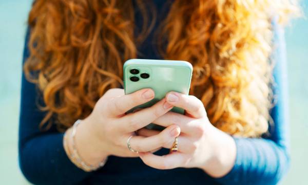 Woman with long red hair holding and looking down at a smartphone.