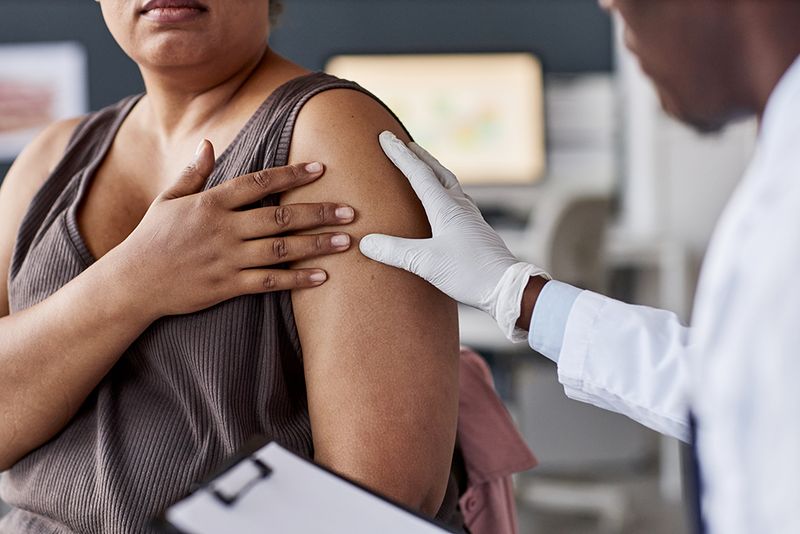 Over shoulder shot of African American doctor examining female patient in clinic and looking at skin rash on arms and shoulders copy space