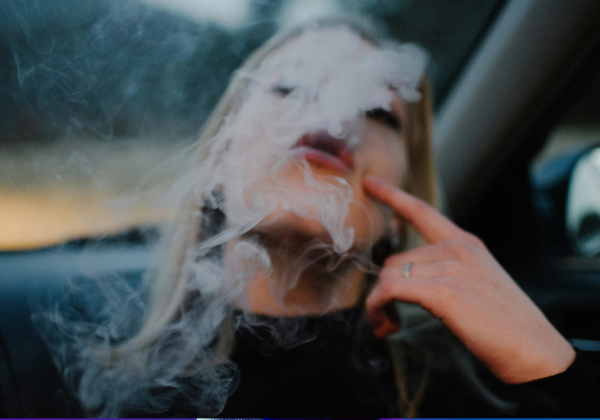 Person smoking and exhaling smoke, illustrating the effects of smoking on skin health and premature aging.