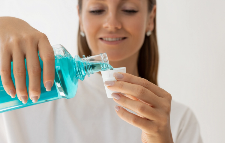 Woman smiling while pouring blue mouthwash from the bottle into a small white cap