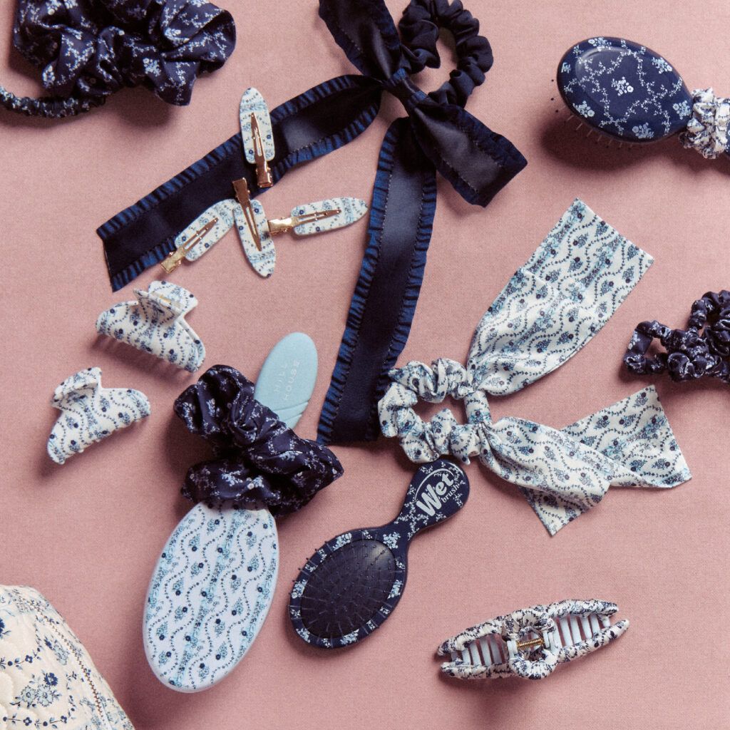 Assortment of Hill House Home x Wet Brush hair accessories and brushes arranged on a pink background, featuring navy and ivory floral prints on scrunchies, bows, claw clips and Wet Brush hairbrushes.