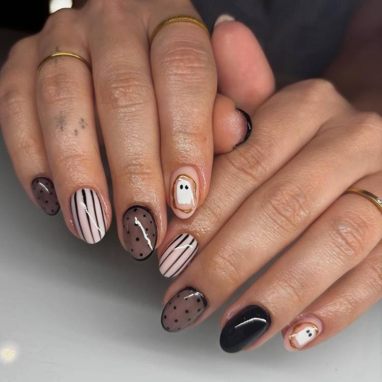 Minimalist Halloween nails with black polka dots, pinstripes, and small gold-outlined ghosts on short oval nails.