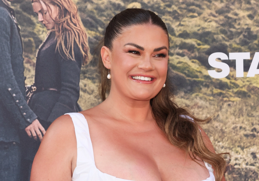 Brittany Cartwright smiles at a red carpet event wearing a white dress and pearl drop earrings