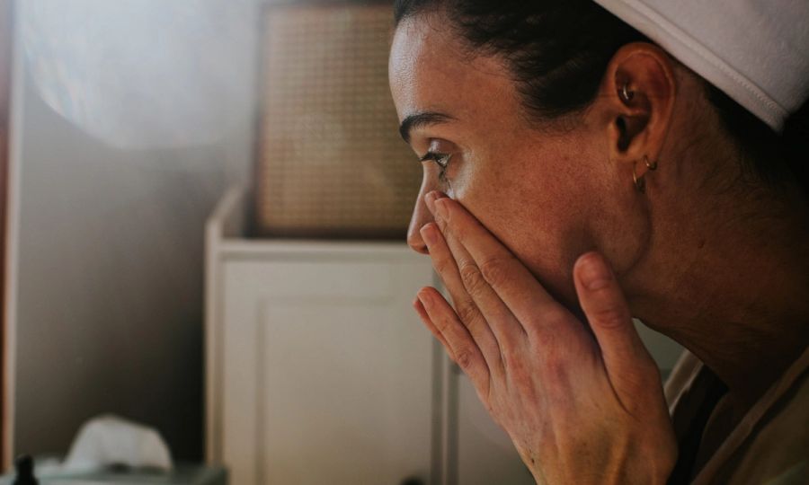 A woman uses her hands to gently pat the skin around her eyes and cheeks, applying beauty products.