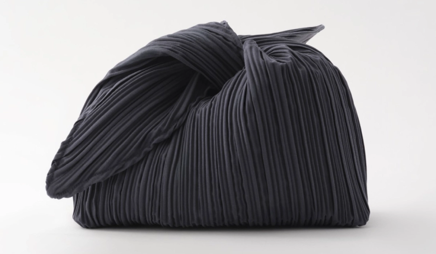 MERIT Beauty's signature makeup bag in dark navy, pleated fabric with a soft, sculptural knotted bow at the top, shown against a plain light background