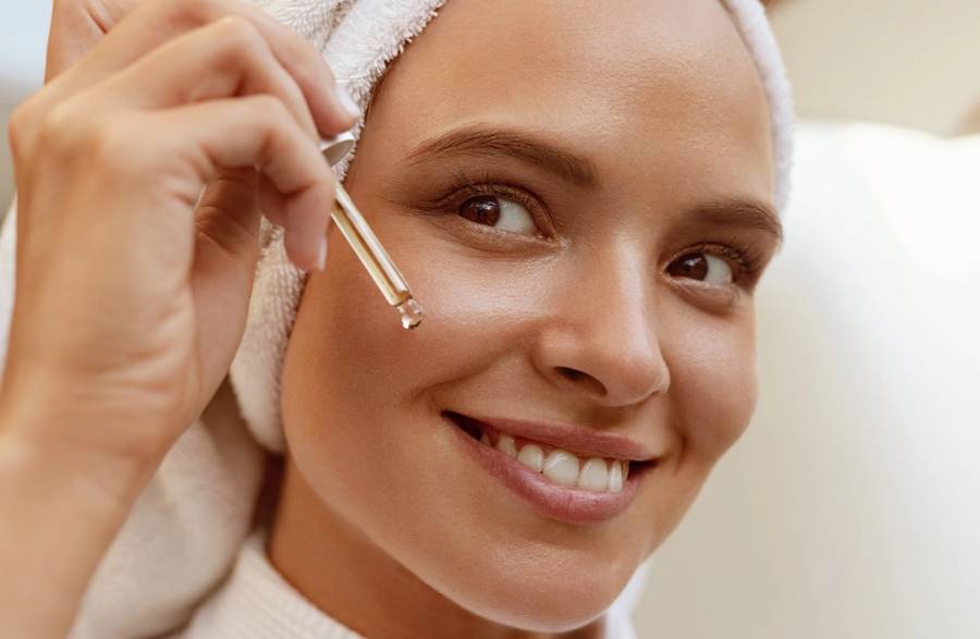 woman using skin serum dropper on cheek