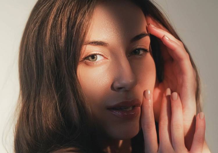 12:05 PM A woman with glowing, even-toned skin holds her hand to her face in warm light