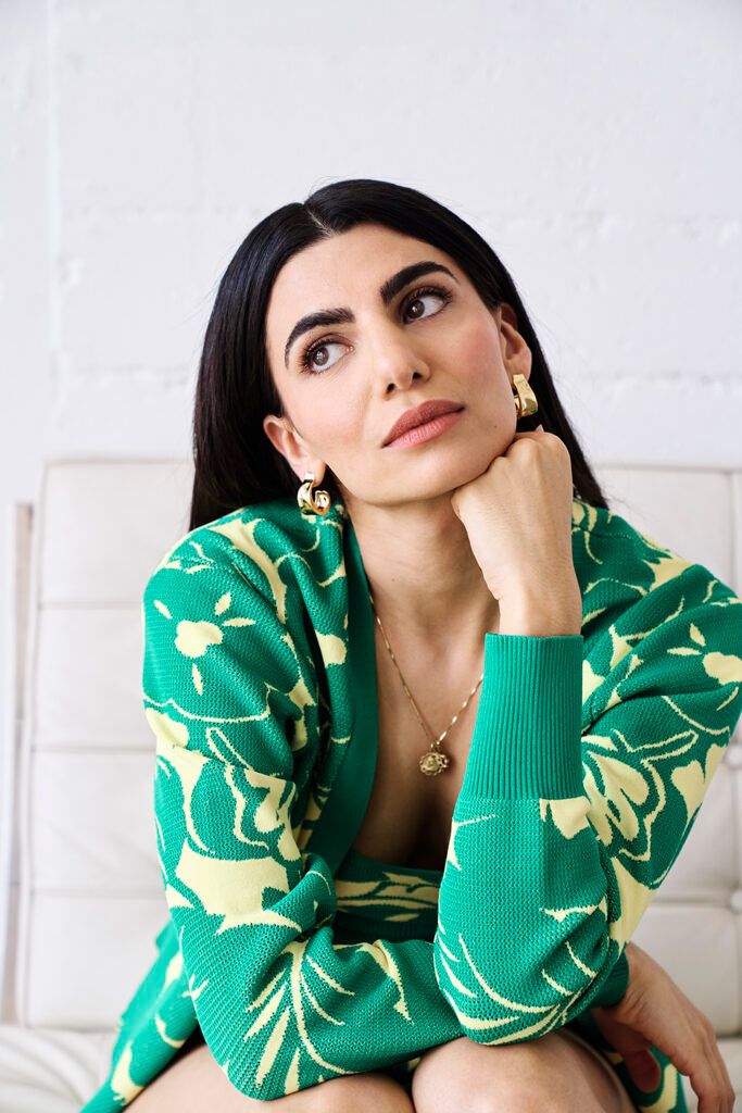 Claudia Doumi sitting with her hand under her chin in green outfit