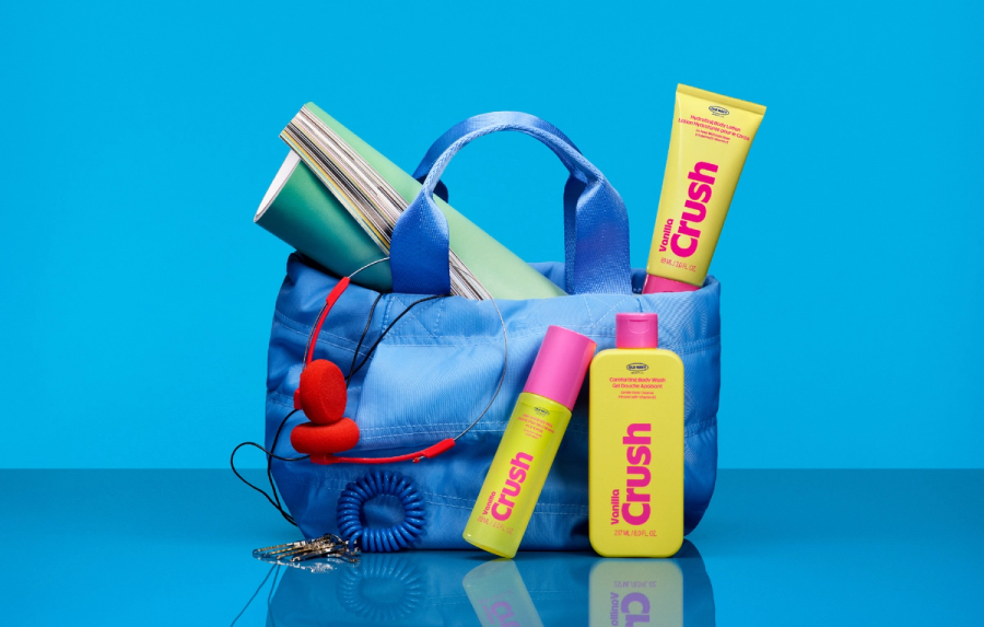 Product photo on a bright blue background: a light blue quilted tote bag with a magazine, red wired headphones, and a coiled keychain spilling out of it.