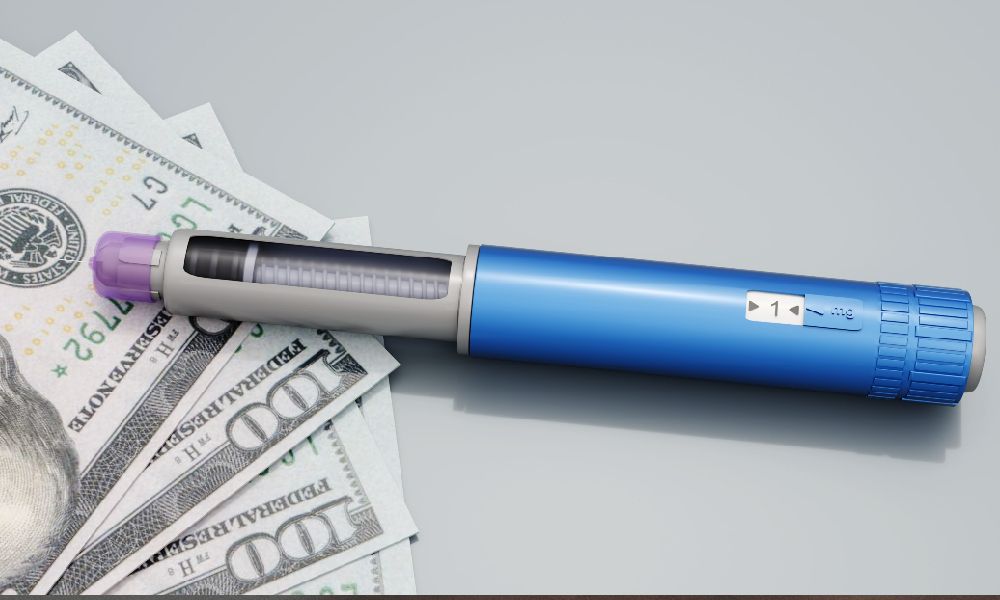 A blue GLP-1 injection pen resting on top of U.S. dollar bills, symbolizing the cost of prescription weight-loss medications