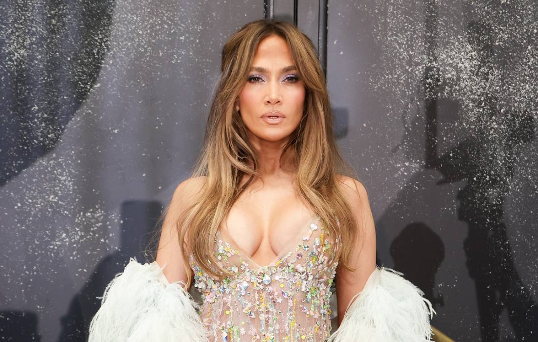 Jennifer Lopez poses in a crystal-embellished nude gown with a white feathered wrap and long, softly waved hair.
