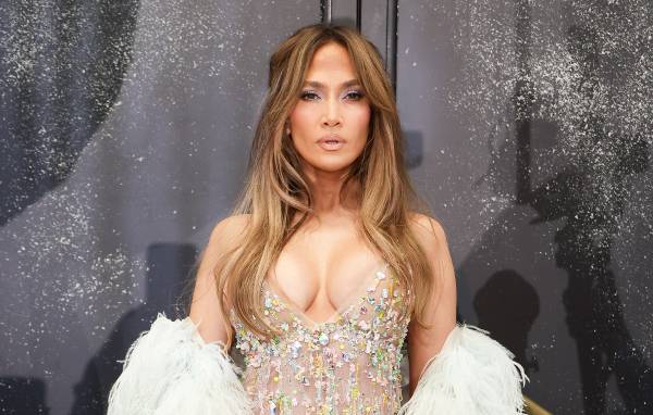 Jennifer Lopez poses in a crystal-embellished nude gown with a white feathered wrap and long, softly waved hair.