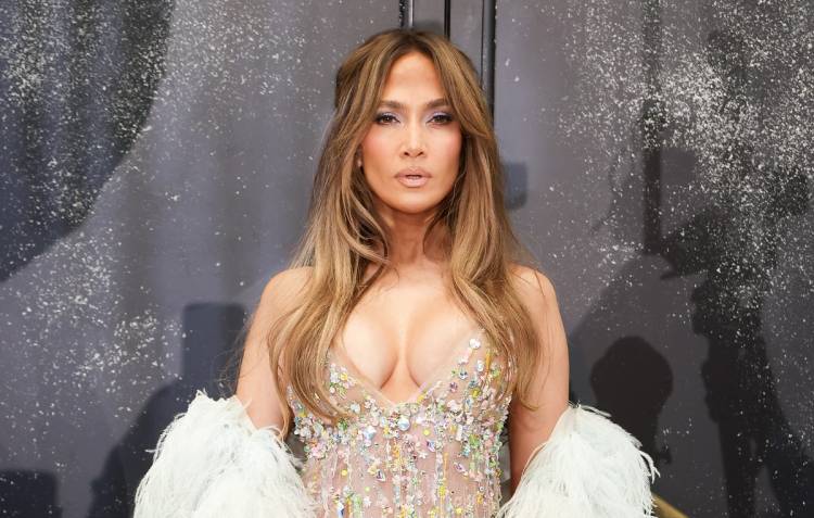Jennifer Lopez poses in a crystal-embellished nude gown with a white feathered wrap and long, softly waved hair.