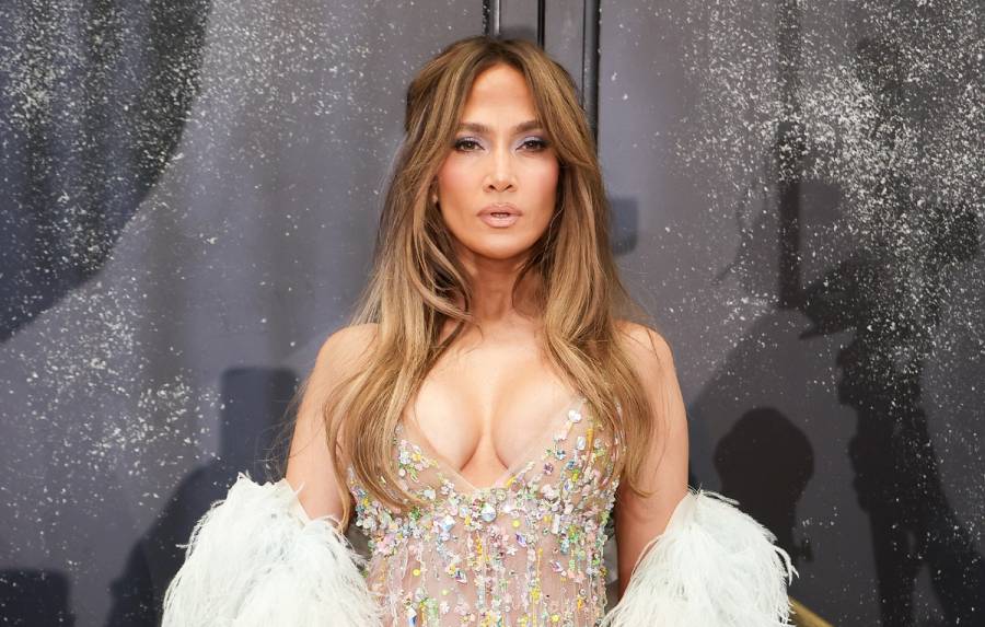 Jennifer Lopez poses in a crystal-embellished nude gown with a white feathered wrap and long, softly waved hair.