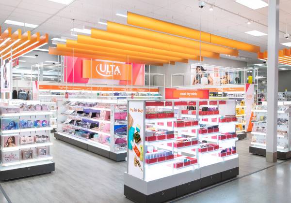 Interior view of an Ulta Beauty shop-in-shop at a Target store, featuring the branded orange overhead signage and lighting, open sightlines to surrounding makeup, skincare, and haircare displays, and a central "must-try minis" endcap stocked with travel-size beauty products