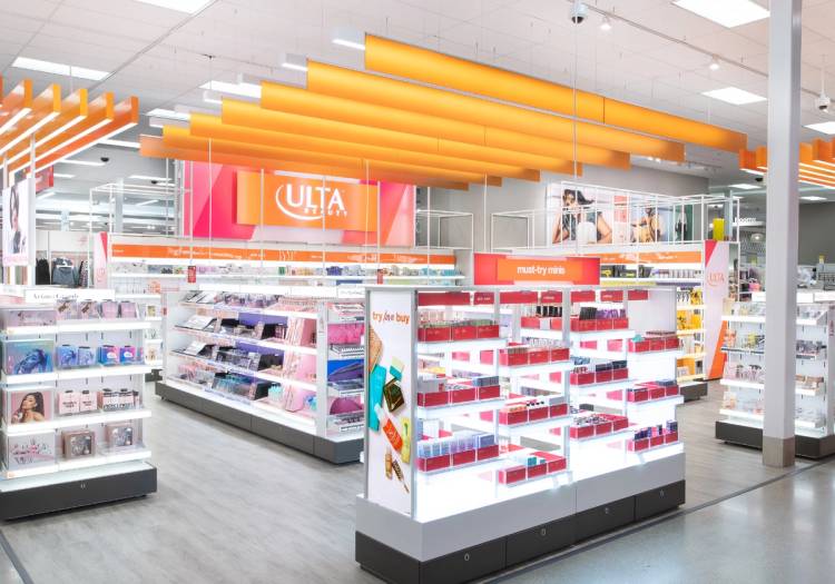 Interior view of an Ulta Beauty shop-in-shop at a Target store, featuring the branded orange overhead signage and lighting, open sightlines to surrounding makeup, skincare, and haircare displays, and a central "must-try minis" endcap stocked with travel-size beauty products