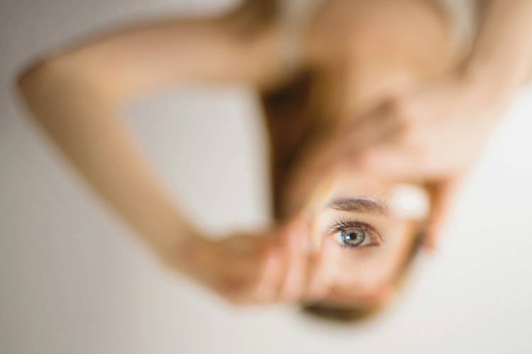 Close-up of a woman’s blue-gray eye and brow reflected in a small handheld mirror, with the background softly blurred