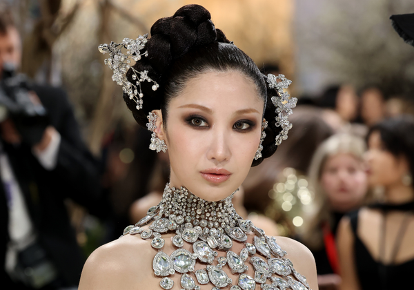 Ejae poses at the Met Gala wearing an embellished black MÔNOT gown with diamond jewelry, ornate crystal hair accessories and glowing skin.