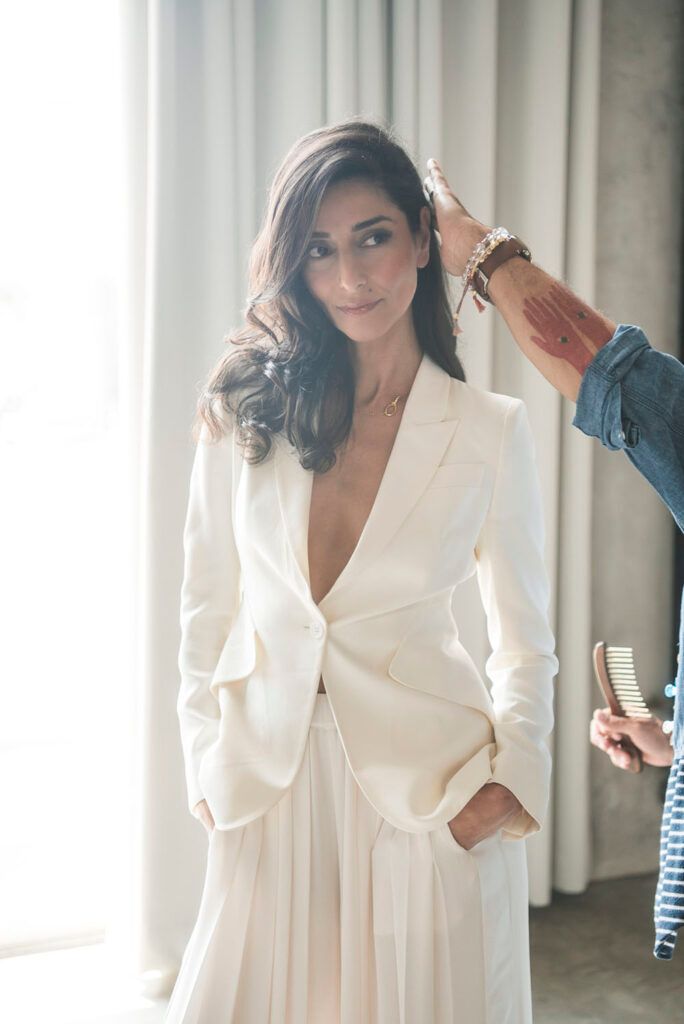 Necar Zadegan in a white blazer and skirt getting her hair fixed up during a photo shoot.