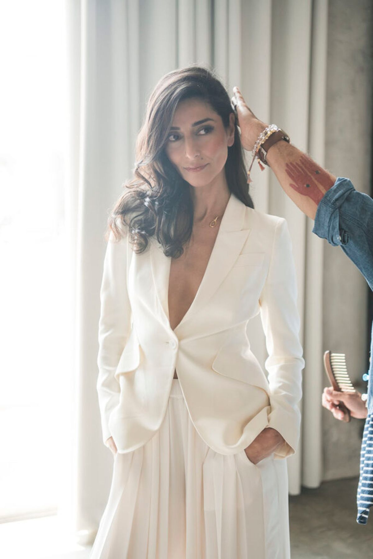 Necar Zadegan in a white blazer and skirt getting her hair fixed up during a photo shoot.