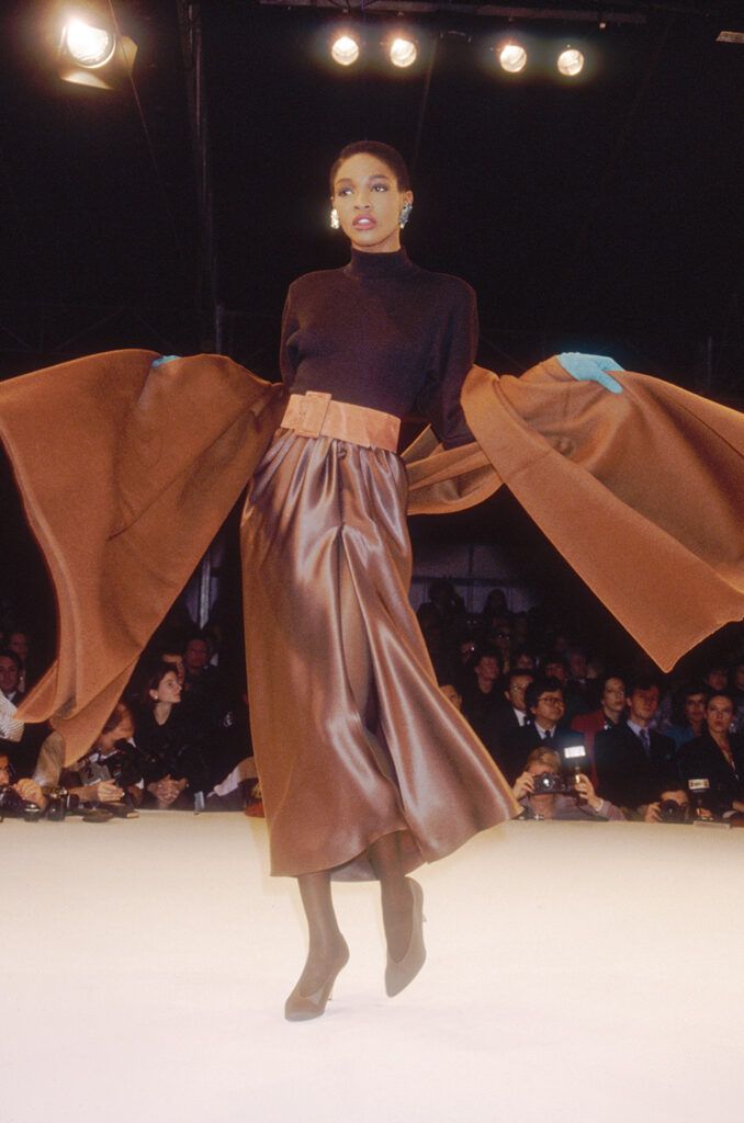 Fashion model Roshumba wears a ready-to-wear sweater and skirt with a matching belt and wrap by French fashion designer Yves Saint Laurent. She is modeling the outfit during his Autumn-Winter 1988-1989 fashion show in Paris.