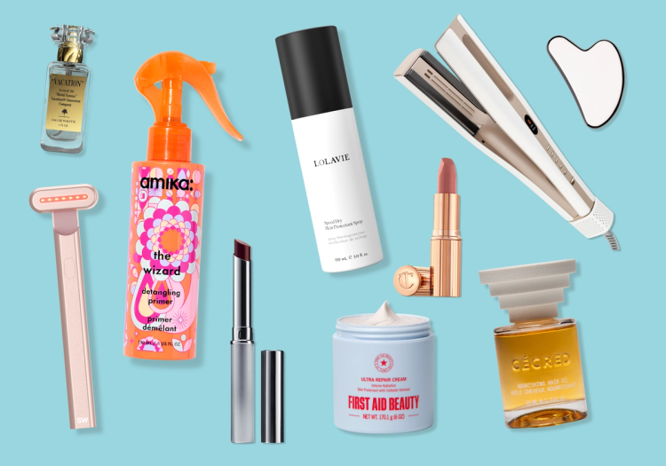 A flatlay of beauty products on a light blue background, including Vacation Eau de Toilette, Amika The Wizard detangling primer, LolaVie heat protectant spray, a hair straightener, a gua sha tool, a pink at-home laser device, a dark red lipstick, Charlotte Tilbury lipstick, First Aid Beauty Ultra Repair Cream and CÉCRED nourishing hair oil.