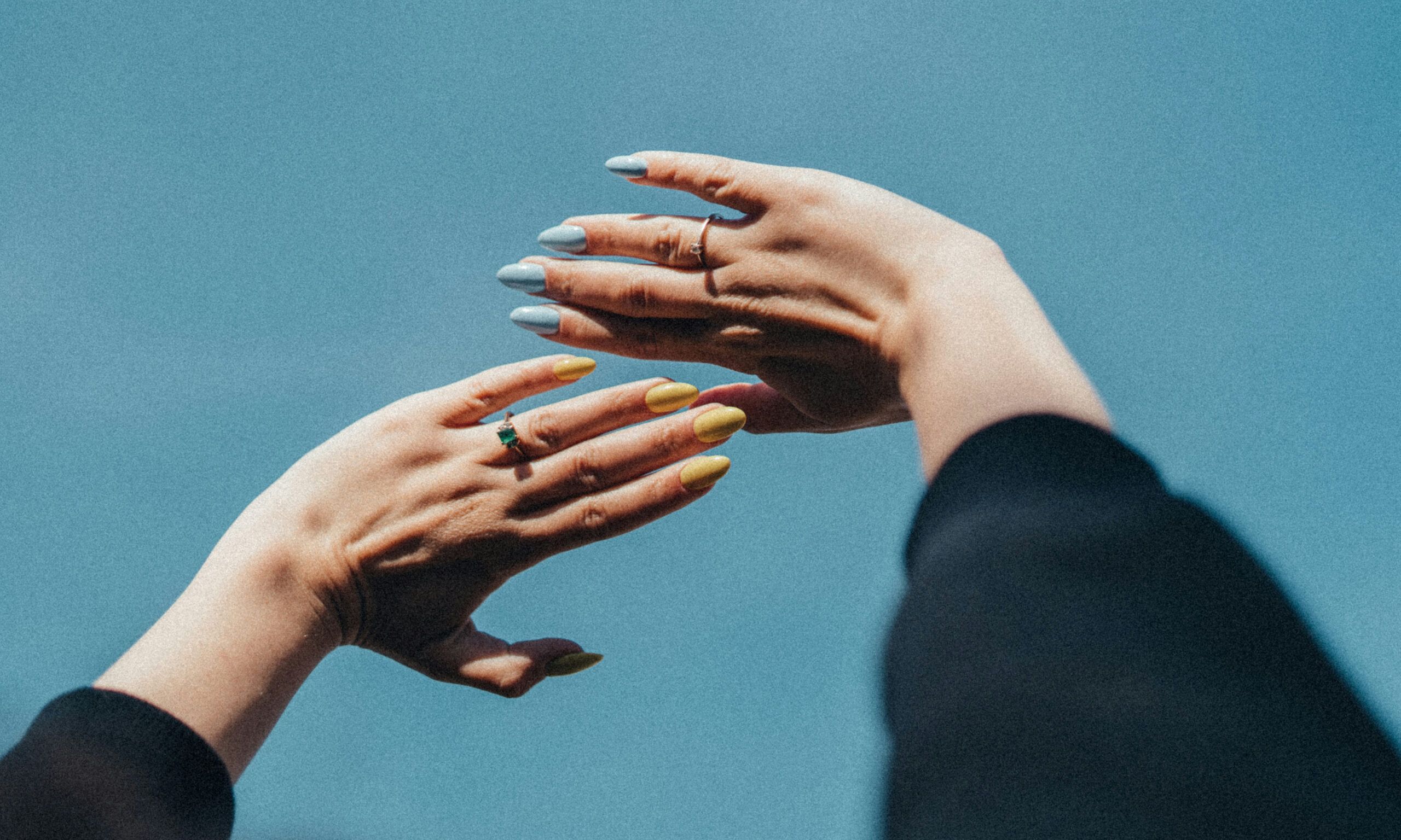 two hands with blue and yellow nail polish holding hands up to the blue sky