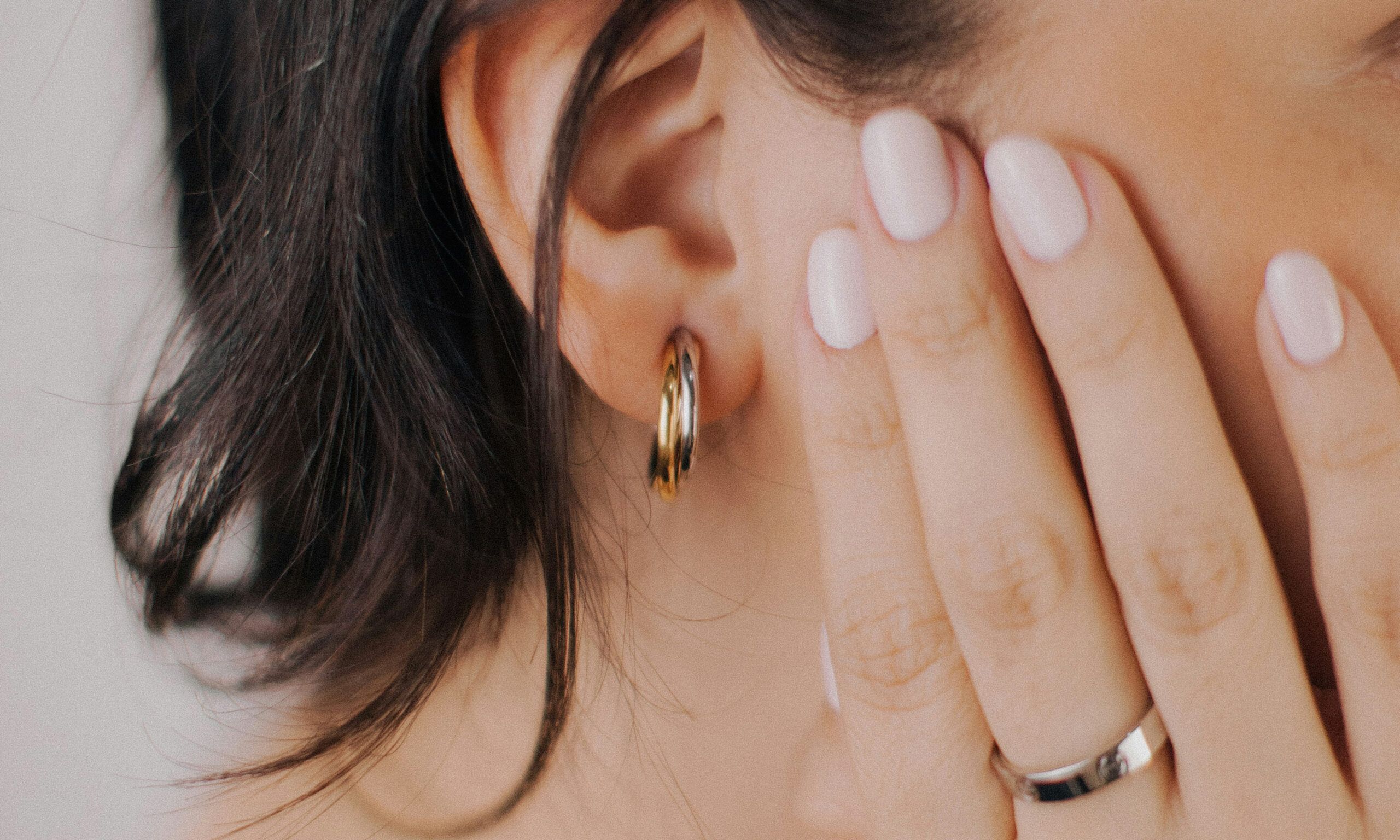 hand with neutral nail polish next to ear