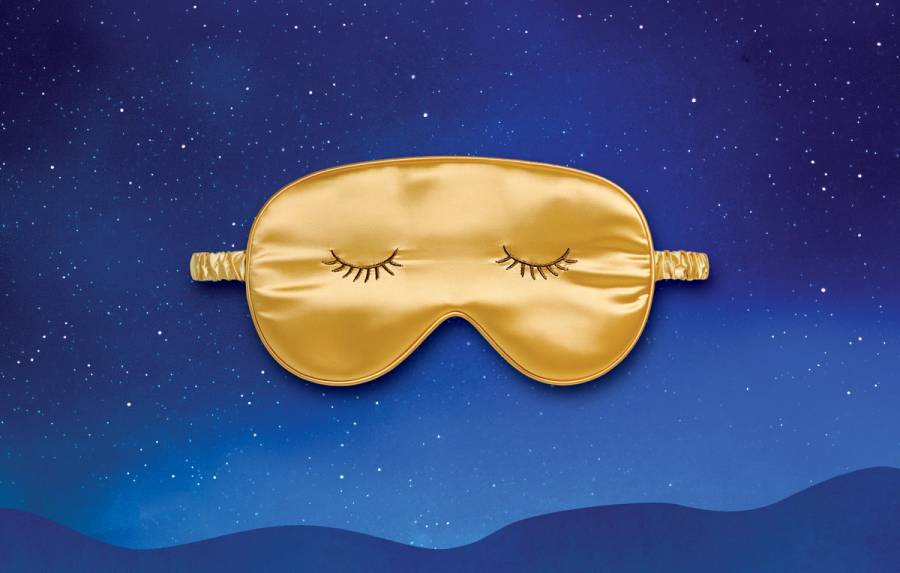Golden satin sleep mask with embroidered closed eyes against a blue, starry night-sky background.