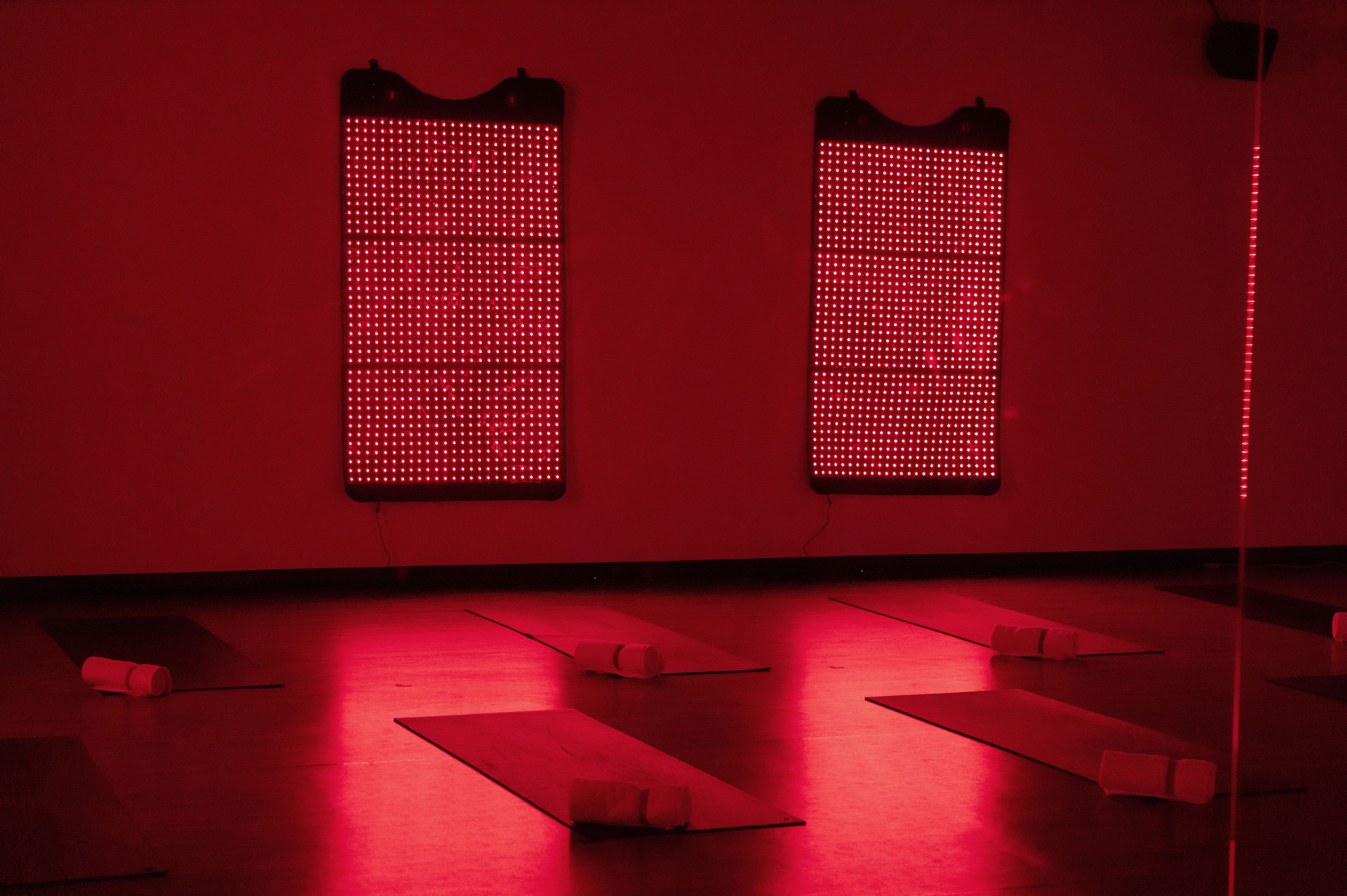 CorePower Yoga studio set up for a red light class, with yoga mats on the floor and HigherDOSE red light therapy panels glowing on the walls.