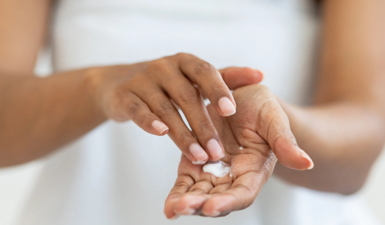 Close-up of a woman applying a dollop of white moisturizer into the palm of her hand