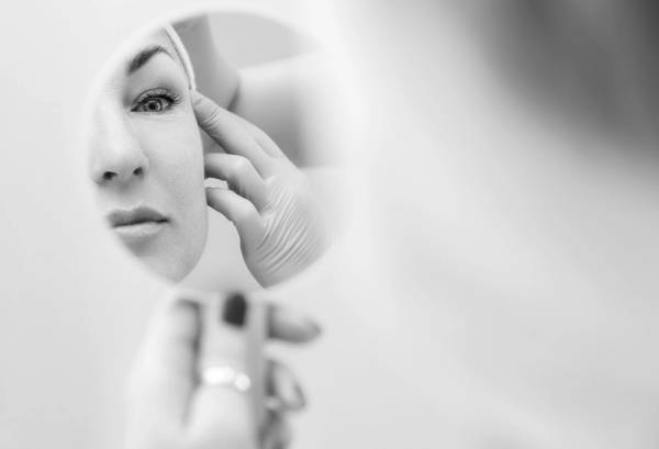 black and white image of woman looking at face in mirror