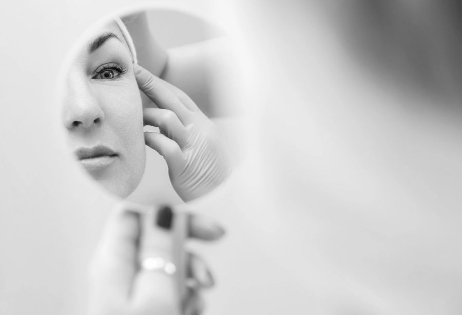 black and white image of woman looking at face in mirror