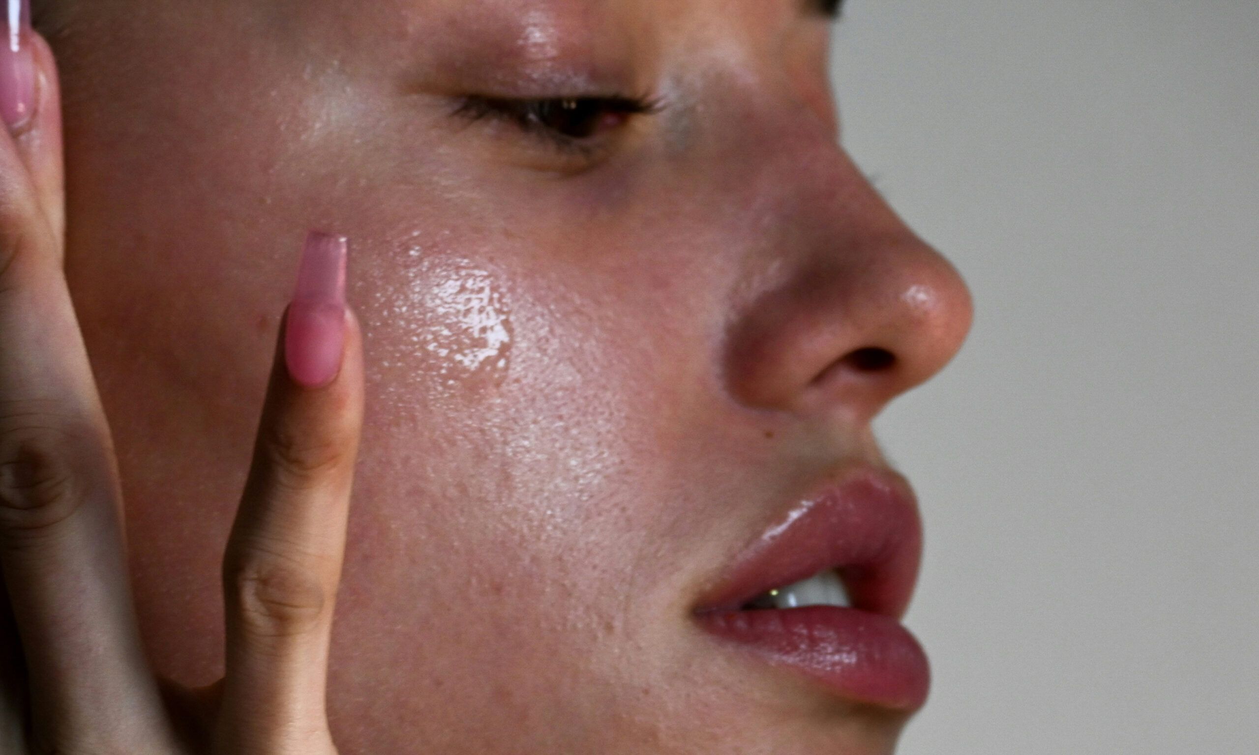 Close side view of woman applying a skin serum on cheek