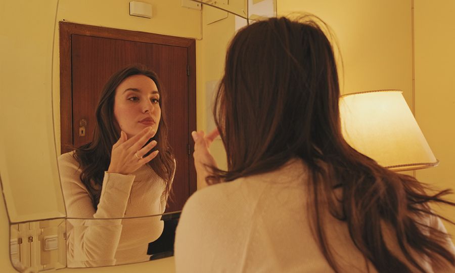 Young woman dressed in coat looks in the mirror