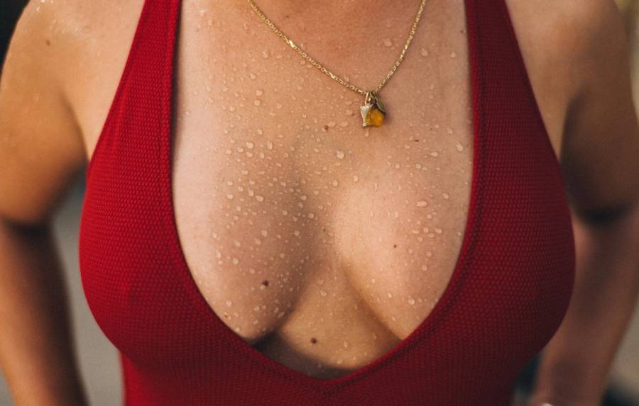 Close-up of a person wearing a red swimsuit and gold necklace, with water droplets across their chest and shoulders.